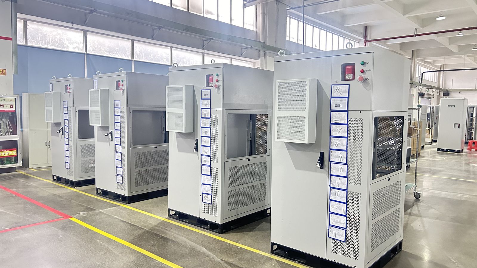 Row of grey commercial battery cabinets staged on the factory floor along yellow marking lines