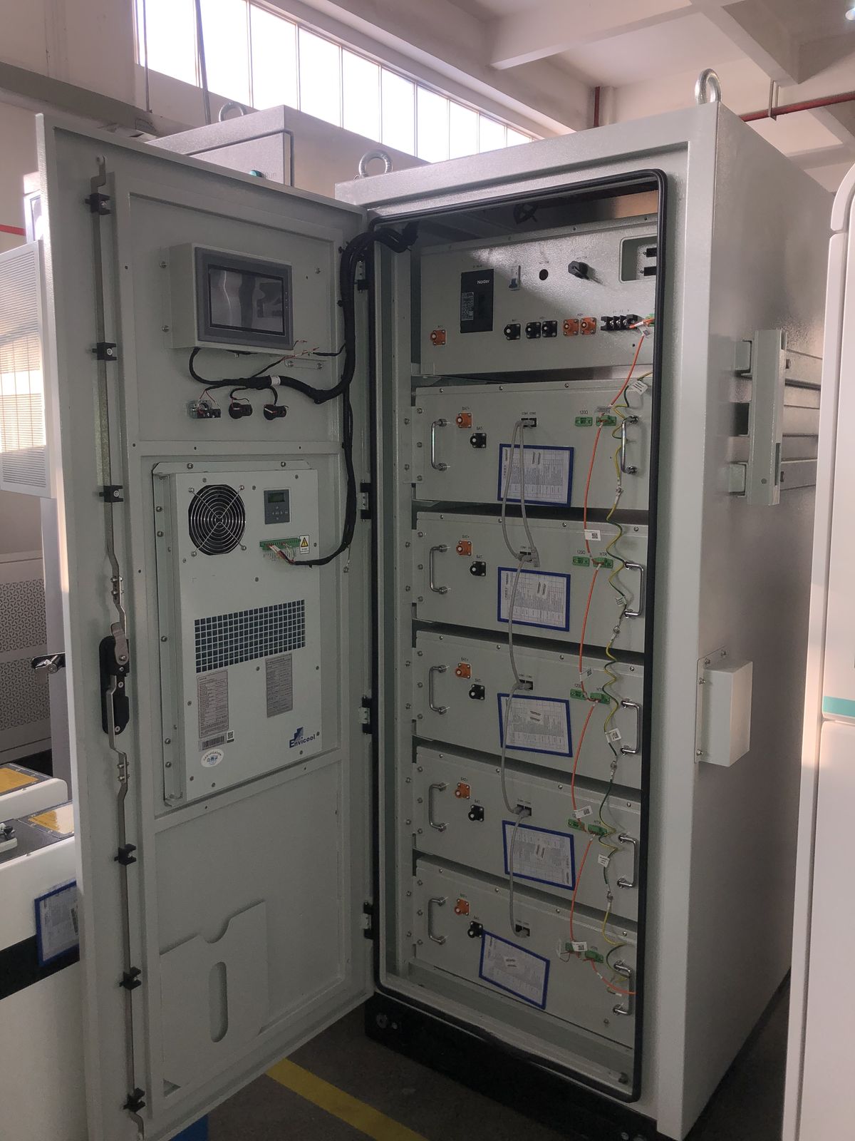 Battery cabinet with door open showing five stacked modules and a door-mounted touchscreen and cooling unit